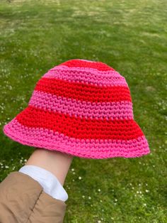 a child's hand wearing a pink and red crocheted hat on top of green grass