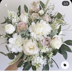 a bouquet of white and pink flowers in someone's hand with green leaves on it