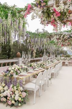 a long table set up with white chairs and flowers hanging from it's ceiling