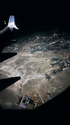 the wing of an airplane flying over a city at night with clouds and lights below