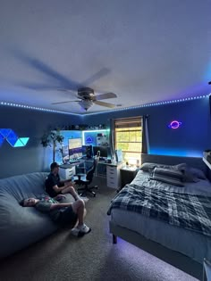 a man sitting on top of a bed in a bedroom next to a computer desk