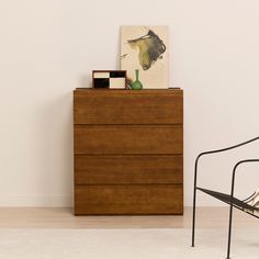 a wooden dresser sitting next to a chair in a room with a painting on the wall