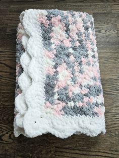 a crocheted blanket on top of a wooden floor with white and pink flowers