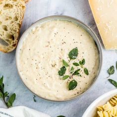 a bowl filled with cream cheese soup next to slices of bread and parmesan cheese