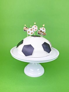 a cake decorated with soccer balls on top of a white platter and topped with candles