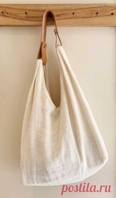 a white linen bag hanging on a wooden hanger with a leather hook in front of it