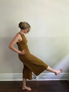 a woman standing on one leg with her legs spread out in the air while wearing a brown dress