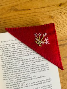 an open book sitting on top of a wooden table next to a red felt triangle