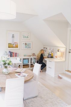 a woman sitting at a table in a room with white furniture and pictures on the wall