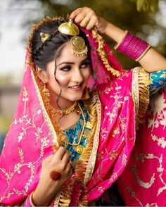 a woman wearing a pink and gold sari with jewelry on her head is smiling at the camera