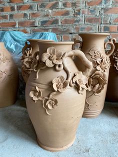 three vases with flowers on them sitting next to each other in front of a brick wall