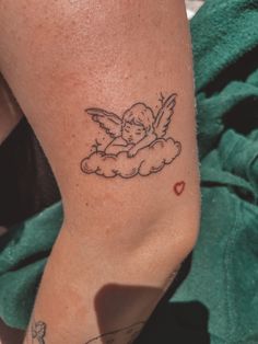 a small tattoo on the leg of a woman with an angel in the sky above her head