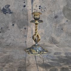 a metal candle holder sitting on top of a stone floor next to a cement wall