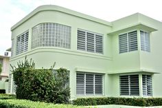 a green house with white shutters on the windows and bushes in front of it