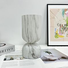 a white vase sitting on top of a table next to books and magazines with pictures in the background