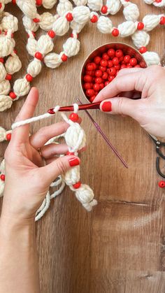 two hands crocheting red and white balls of yarn with scissors on a wooden table