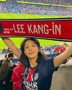 a woman holding up a scarf in front of a crowd at a soccer game with the words lee kang - in written on it