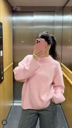 a woman taking a selfie in an elevator wearing a pink sweater and grey pants