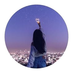 a woman holding up a heart shaped object in front of a cityscape at night