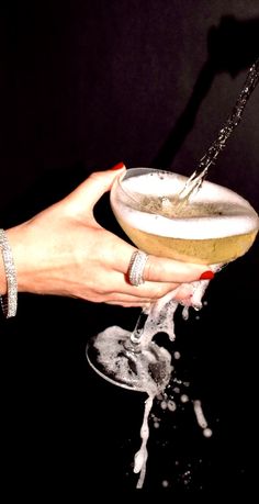 a woman holding a wine glass with water pouring out of it and her hand on the rim