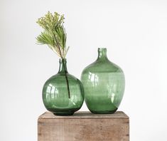 two green vases sitting on top of a wooden box next to each other and one has a plant in it