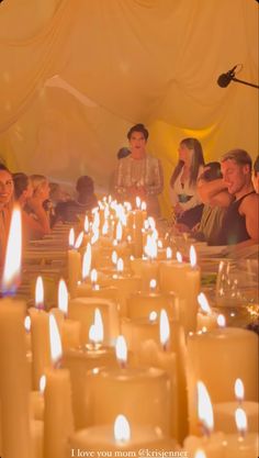 many people are sitting at a long table with candles in front of them