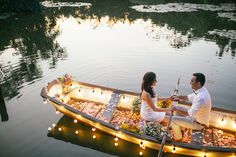 a man and woman sitting in a boat with food on the water at night time