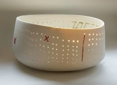 a close up of a white bowl with red writing on the side and holes in it