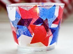 a red, white and blue candle is sitting in a glass cup with stars painted on it