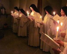 a group of women in white robes holding candles and reading paper with words on them