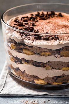 a layered dessert with chocolate chips and cream in a glass dish on top of a napkin