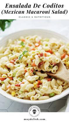 a white bowl filled with macaroni salad next to a wooden spoon