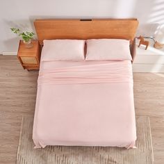 a bed with pink sheets and pillows on top of it in a room next to a wooden headboard