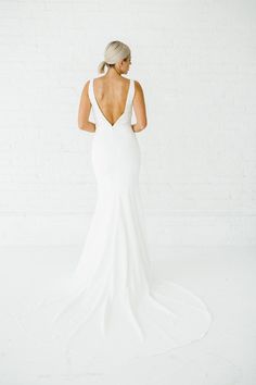 a woman in a white wedding dress standing against a brick wall with her back to the camera