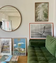 a living room with green couches and pictures on the wall above them, along with a round mirror