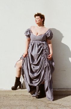 a woman in a gray dress leaning against a wall