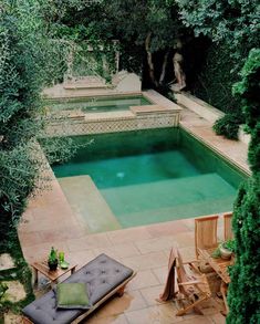 an outdoor swimming pool surrounded by trees and lawn chairs with cushions on the ground next to it