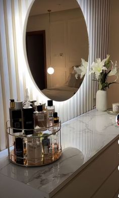 a bathroom vanity with a round mirror above it and bottles on the counter in front of it