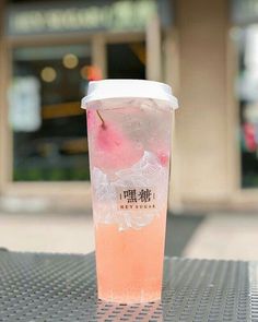 a plastic cup filled with liquid sitting on top of a metal table next to a building