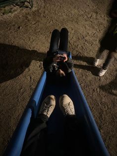 two people standing next to each other near a blue pipe on the ground with their feet up