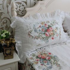 a white bed topped with lots of pillows next to a night stand