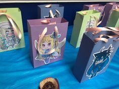 four small bags with designs on them sitting on a blue table cloth next to a cupcake