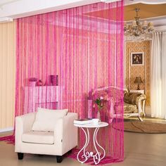 a living room with pink curtains and a white chair in front of a table on the floor