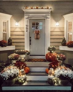 front porch decorated for fall with pumpkins and flowers on the steps, lighted by lights