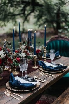 a wooden table topped with plates covered in blue napkins and flowers next to candles