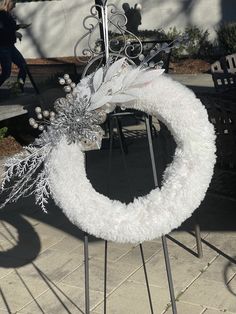 a white wreath is sitting on top of a metal stand with snow flakes around it