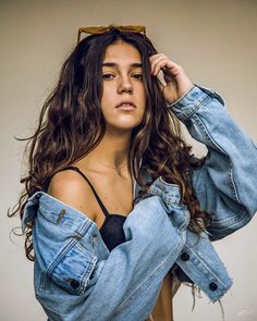 a woman with long hair wearing a jean jacket and black bra top is posing for the camera