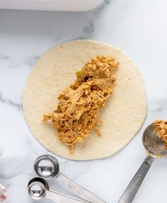 a tortilla with shredded meat on it next to measuring spoons