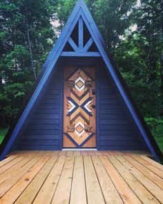 a wooden deck with a triangle shaped door in front of it and trees behind it