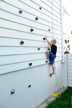 a young boy climbing up the side of a white house with his hands on a rope